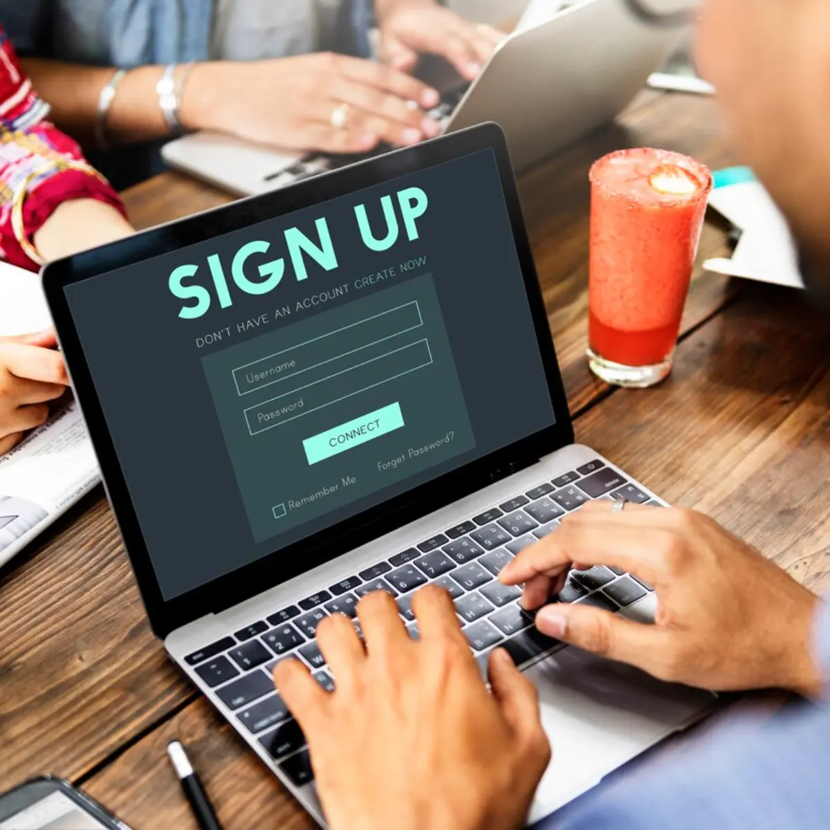 A person types on a laptop displaying a Sign Up page with username and password fields, beside a refreshing drink.