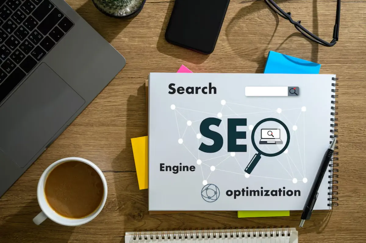 A workspace featuring a laptop, coffee cup, colorful sticky notes, and a notepad with SEO and related terms, emphasizing search engine optimization.
