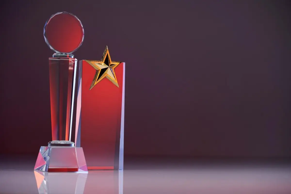 A shiny crystal trophy with a round top and a red base, beside a red plaque featuring a golden star, against a gradient backdrop.