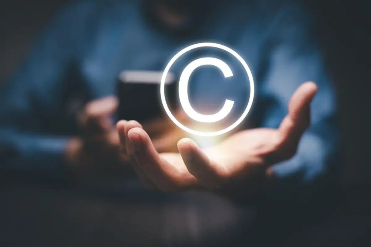 A hand holding a glowing copyright symbol against a dark background, representing digital ownership and intellectual property rights.