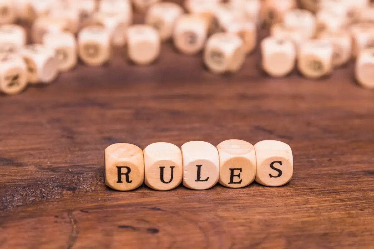 Wooden blocks spell out the word RULES on a rustic wooden surface, surrounded by scattered letter blocks.