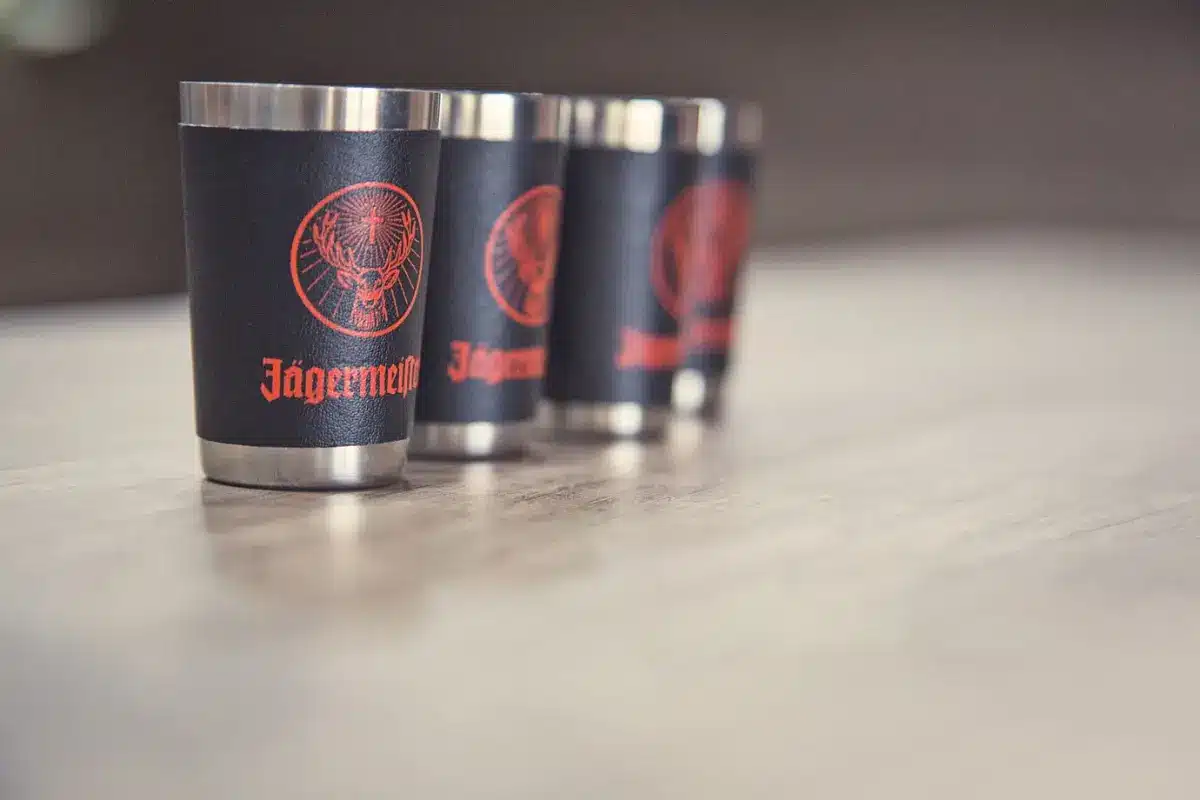 Three metallic shot glasses with black and red Jägermeister branding are lined up on a wooden table.