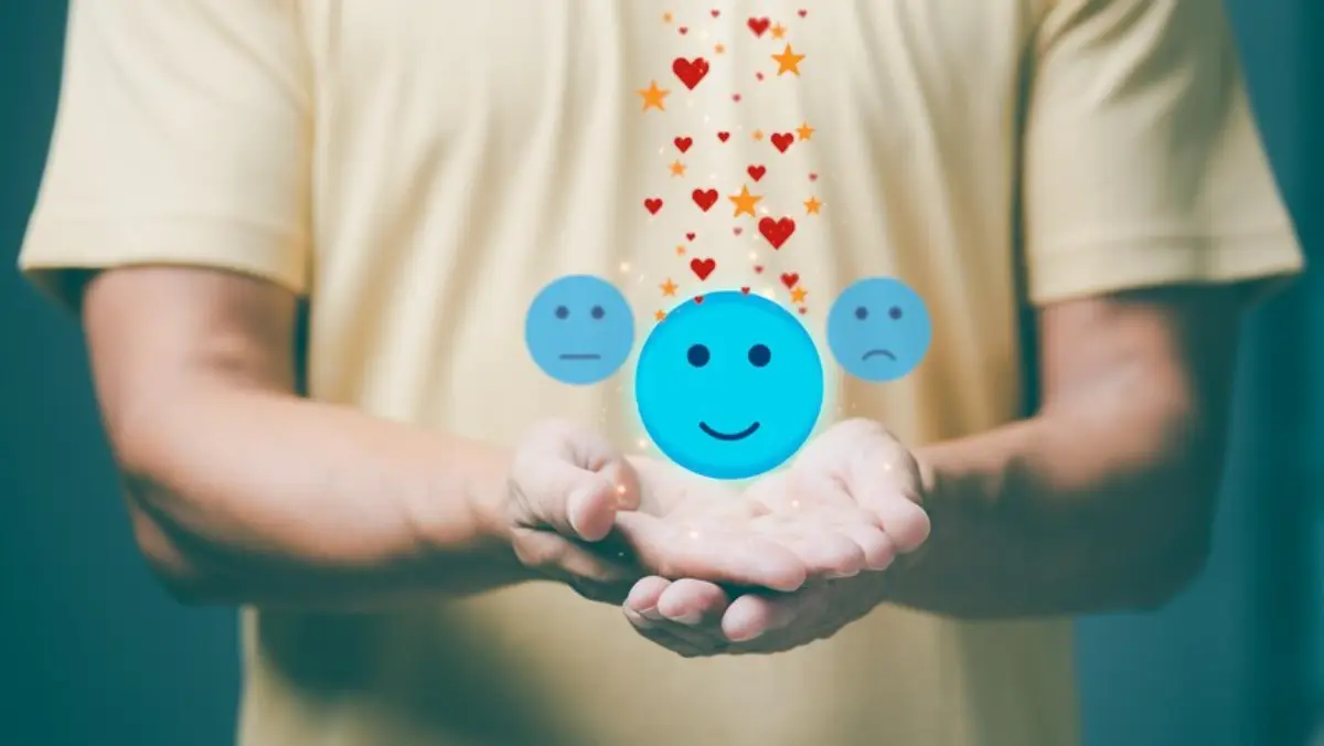 A person holding glowing emoji faces, expressing different emotions, with hearts and stars floating above, symbolizing feelings.