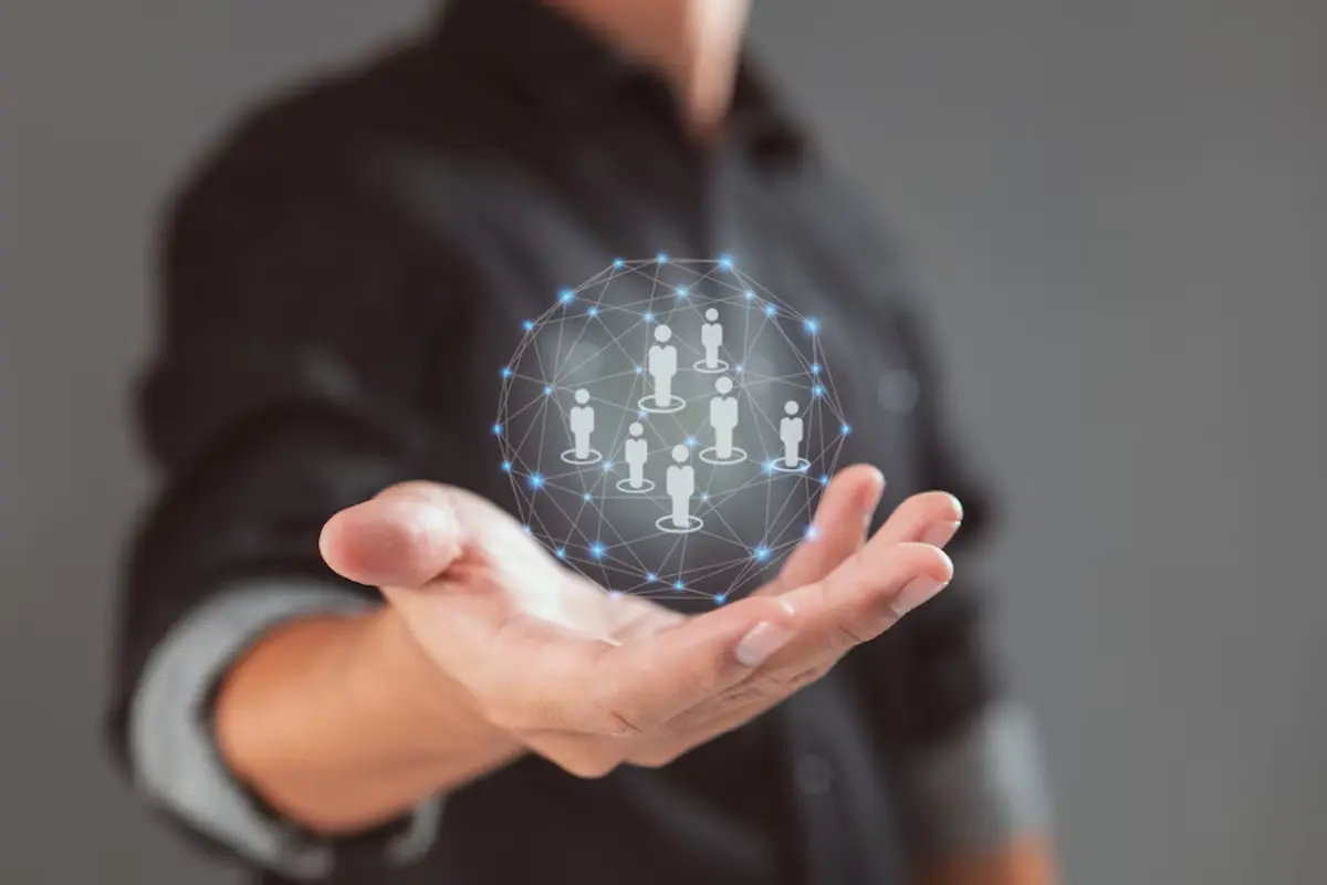 A businessman holds out his hand, displaying a digital network of interconnected figures symbolizing teamwork and collaboration.
