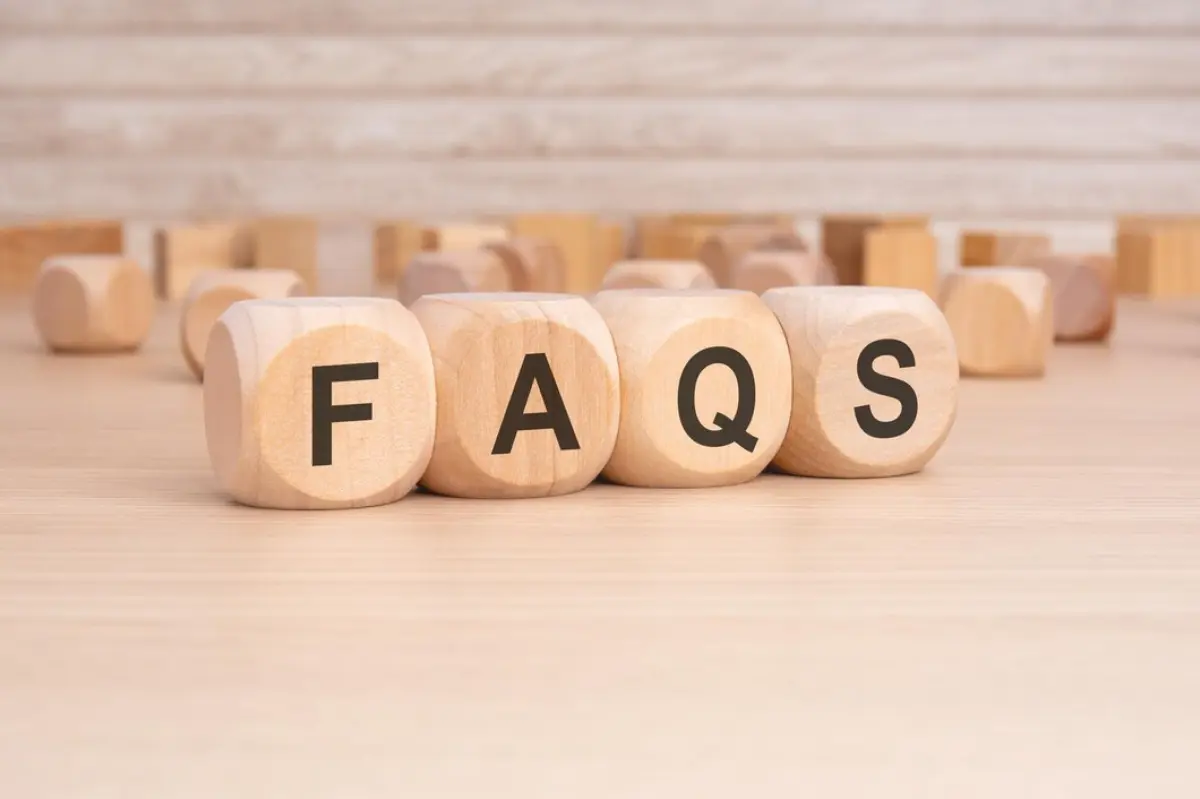 Wooden blocks spelling FAQs on a light wooden surface, with additional blurred blocks in the background.