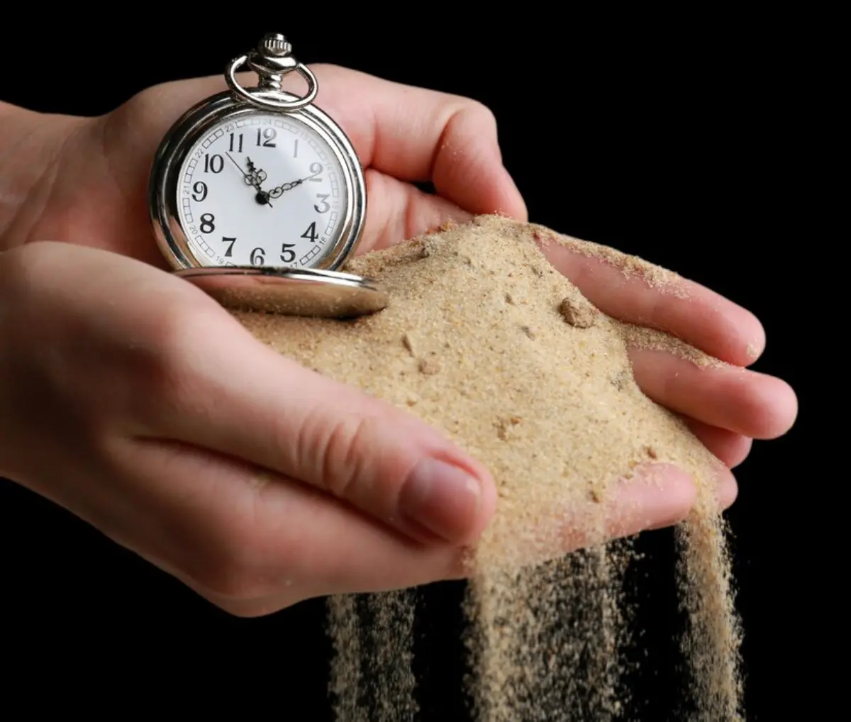A close-up of hands holding sand, with a vintage pocket watch set into the pile, symbolizing the passage of time.