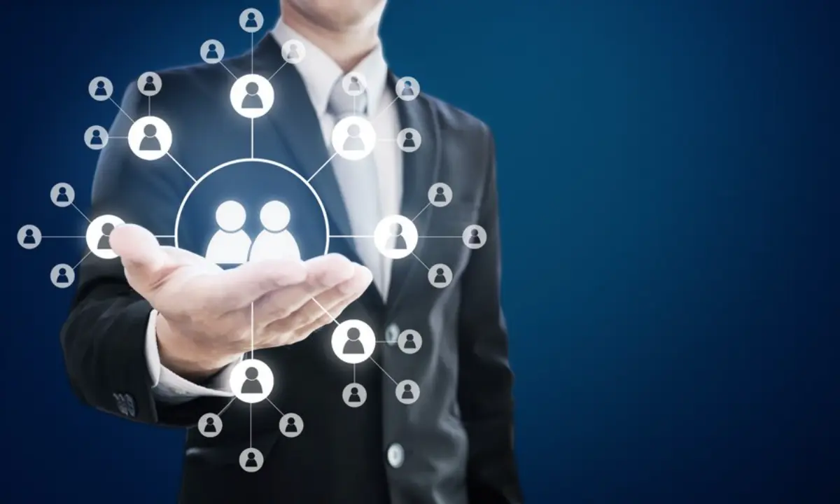 A businessman in a suit holds out his hand, displaying icons of people connected in a network, symbolizing teamwork or networking.
