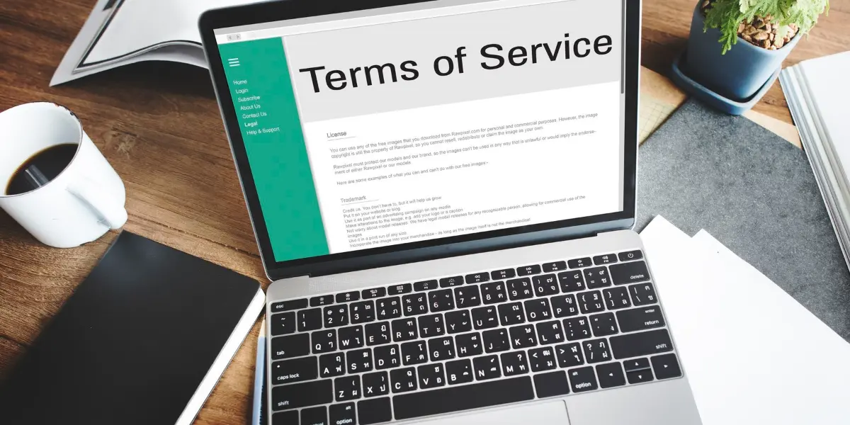 A laptop displaying Terms of Service on a webpage, surrounded by a coffee cup, a notebook, and a plant.