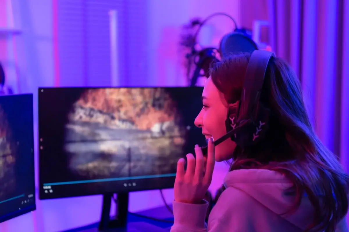 Person in headphones seated at a desk, interacting with a vibrant, glowing computer screen displaying a scenic landscape.