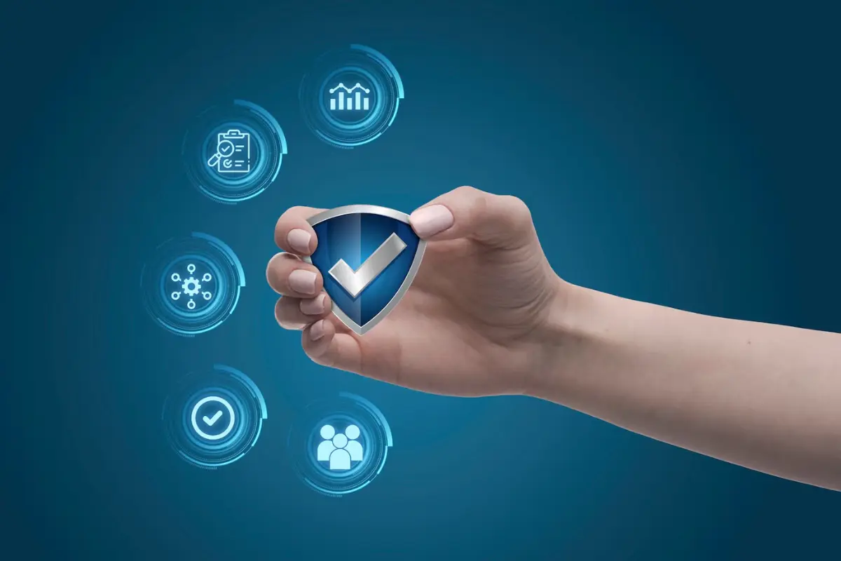 A hand holds a blue shield icon with a check mark, surrounded by various technology and data-related symbols against a blue background.