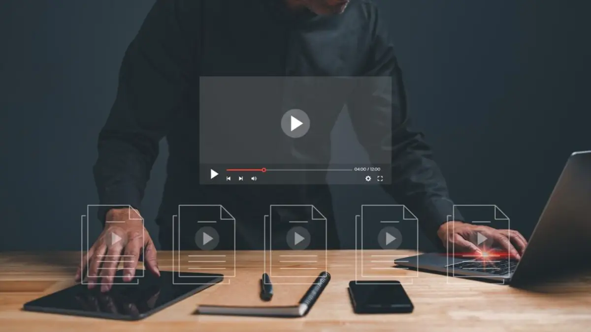 A person in a black shirt interacts with digital devices on a wooden desk, featuring video playback and document icons.