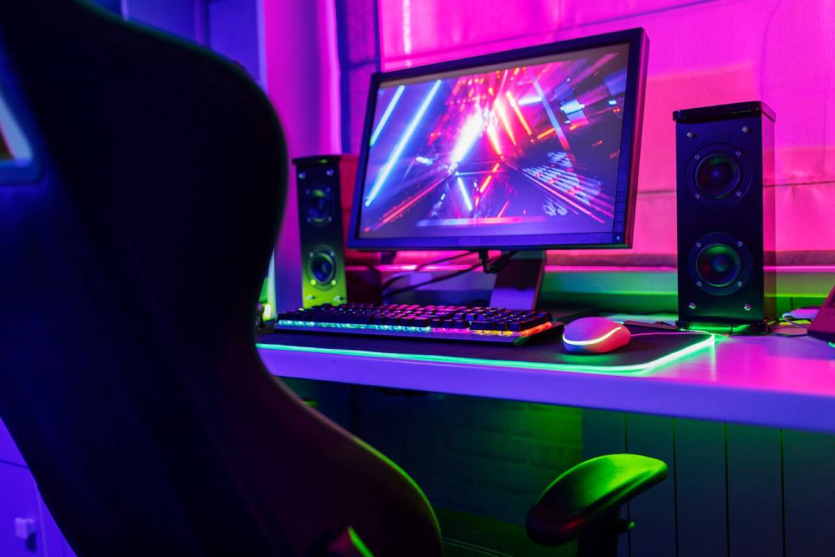 A modern gaming setup featuring a sleek chair, illuminated keyboard, speakers, and a vibrant screen with colorful graphics. 