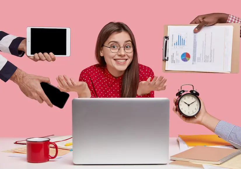A person expresses confusion while surrounded by gadgets, papers, and a clock, indicating a chaotic work environment.
