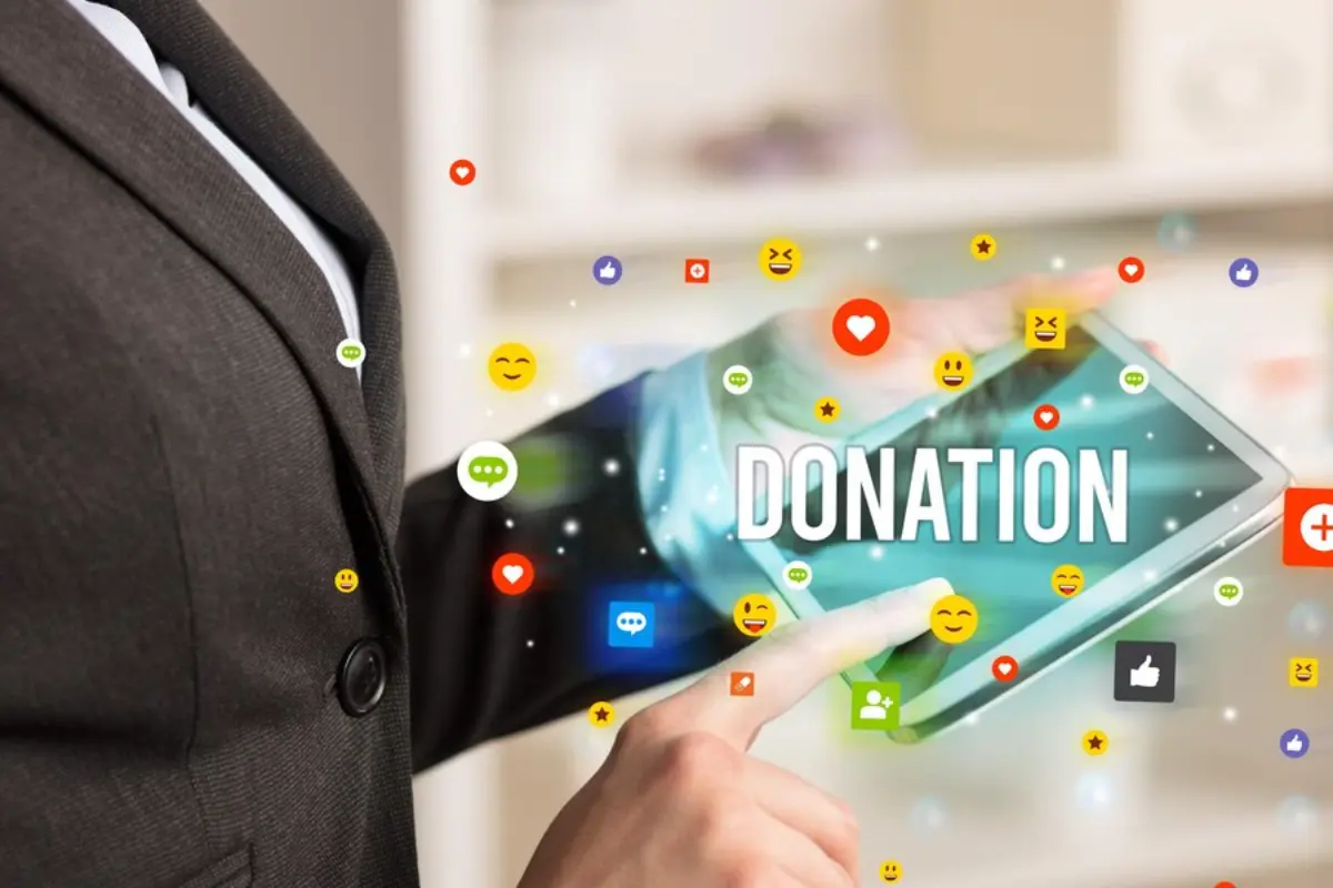 A businessperson uses a tablet displaying the word Donation, surrounded by various social media icons and emojis.