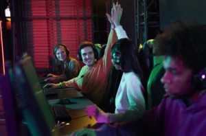 A group of gamers with headsets celebrates a victory, raising their hands in a colorful, illuminated gaming environment.