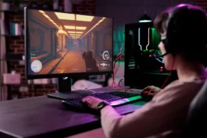 A gamer wearing a headset plays an action game on a desktop monitor, showcasing a virtual corridor scene with targets.